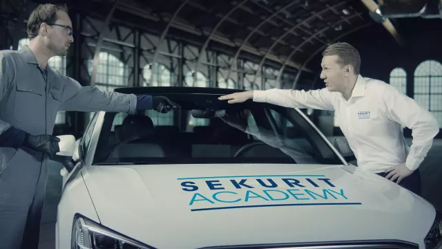 A fitter and a customer next to a Sekurit Academy branded car 